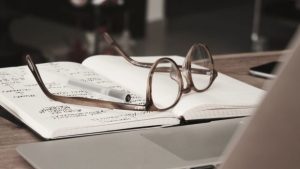 Glasses laying on a book in front of a laptop