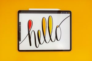 The word hello written in cursive on an iPad in front of a yellow background