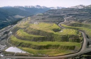 Green tiered hills in front of a mountain backdrop show the site of waste rock dumps at an open pit coal mine after reclamation to wildlife habitat.